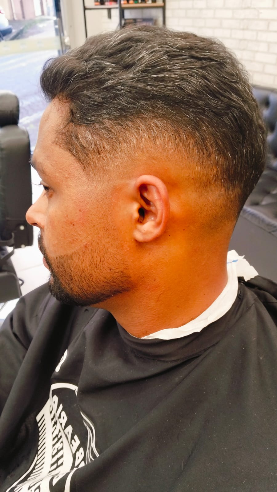 Cliente de perfil com fade lateral, vestindo a camiseta da barbearia